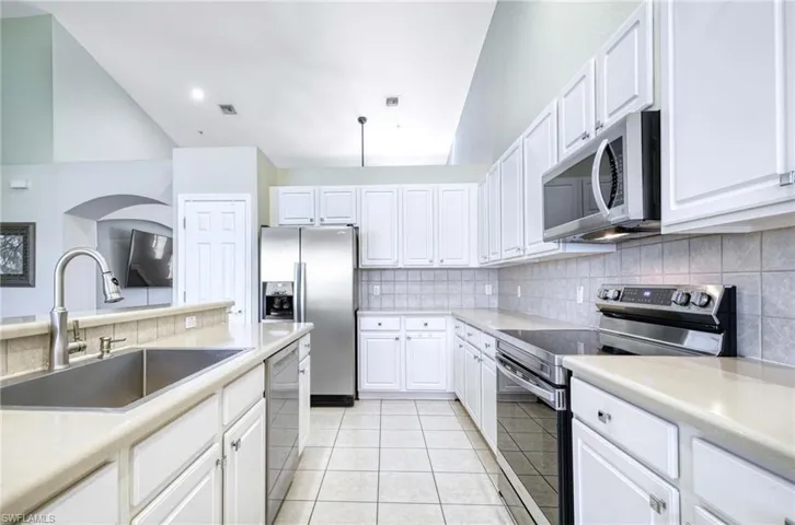 Kitchen featuring stainless steel appliances, a sink, backsplash, white cabinets, and light tile patterned flooring