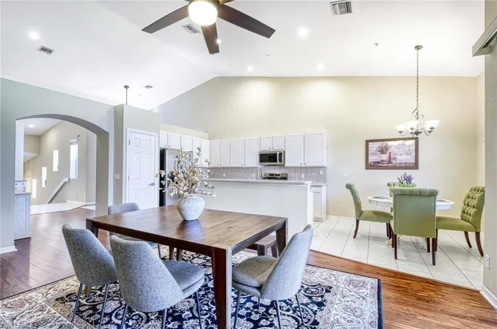 Dining space with arched walkways, ceiling fan, light wood-type flooring, high vaulted ceiling, and a chandelier
