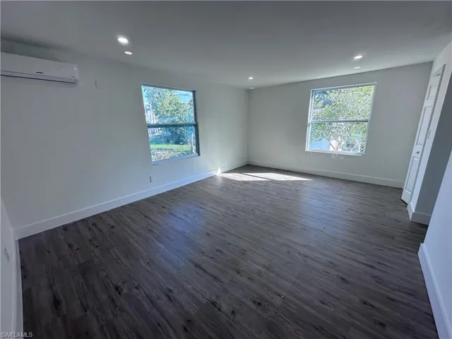 Unfurnished room with an AC wall unit, dark wood-type flooring, baseboards, and recessed lighting