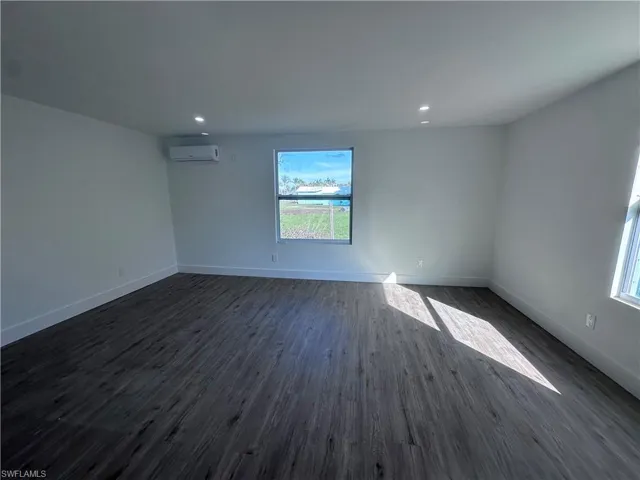 Empty room featuring an AC wall unit, healthy amount of natural light, dark wood-style floors, baseboards, and recessed lighting