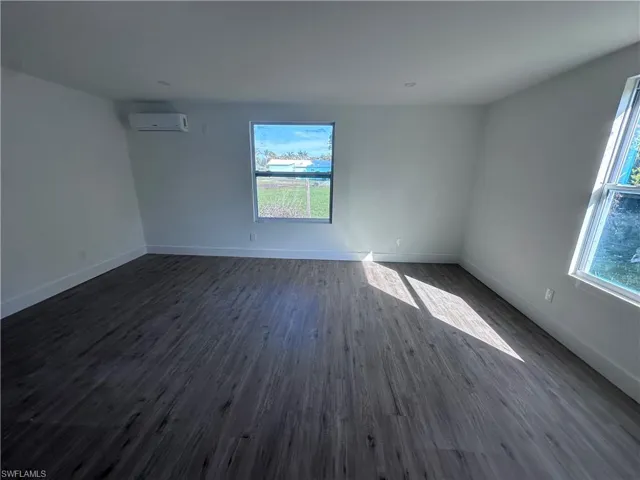 Empty room with an AC wall unit, dark wood-style floors, and baseboards