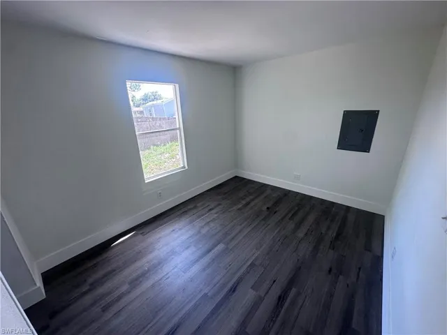 Unfurnished room featuring electric panel, dark wood finished floors, and baseboards