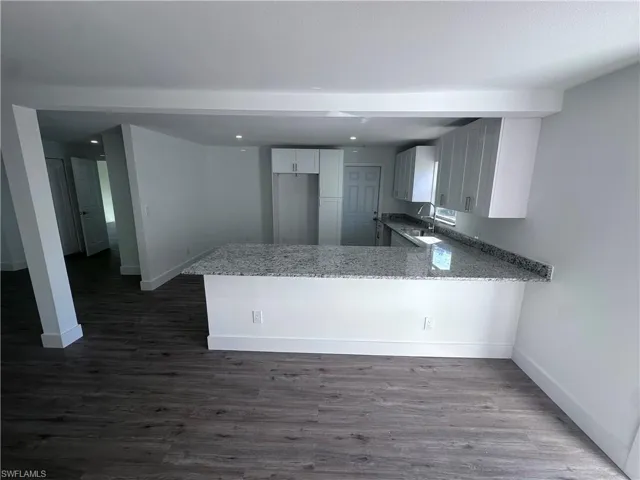 Kitchen featuring a peninsula, baseboards, light stone counters, and dark wood-style flooring