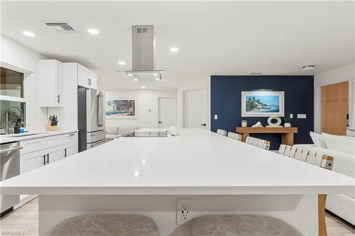 Kitchen with light wood-style floors, a breakfast bar, white cabinets, stainless steel appliances, and island range hood
