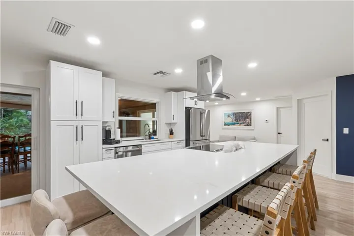 Kitchen featuring a breakfast bar area, light wood finished floors, white cabinets, a large island, and light stone countertops