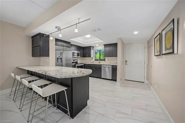 Modern kitchen featuring dark cabinetry, stainless steel appliances, and a light-toned granite countertop island