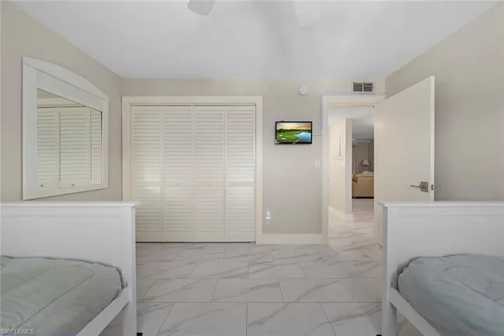 Light-toned room featuring a ceiling fan, louvered bi-fold closet doors, a wall-mounted television, and tile flooring