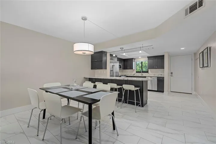 Open-concept living space featuring large format tile flooring, a contemporary drum pendant light, and a kitchen with dark cabinetry, stainless steel appliances, and a breakfast bar with stone countertops