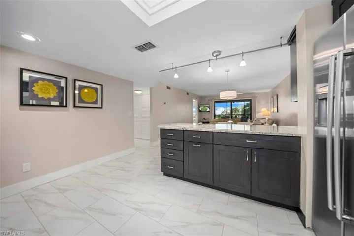 Kitchen island featuring dark cabinetry, light granite-style countertop, and stainless steel refrigerator