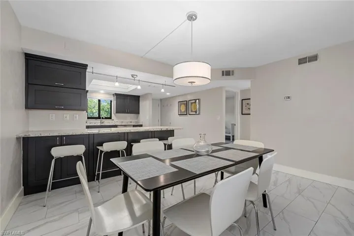 Open-concept dining area featuring light-toned flooring, a drum pendant light fixture, and a pass-through to the kitchen