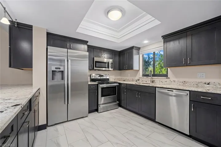 Kitchen featuring dark cabinetry, stainless steel appliances, light-toned countertops, and white tile flooring