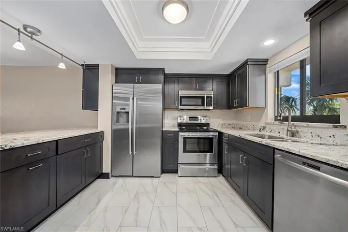 Contemporary kitchen featuring dark wood cabinetry, stainless steel appliances, and light granite-style countertops
