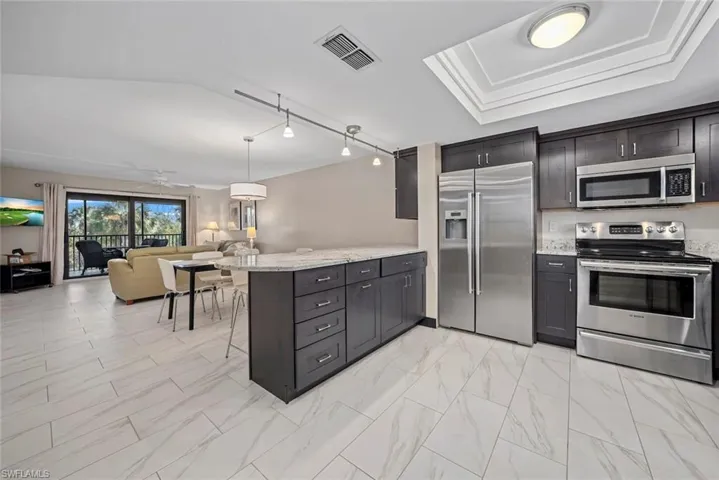 Open-concept kitchen featuring dark wood cabinetry, stainless steel appliances, a center island with a light-toned countertop, and tile flooring