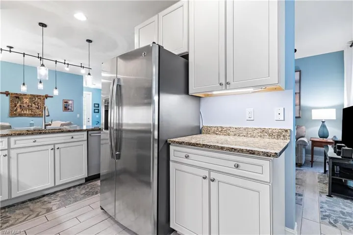 Kitchen with pendant lighting, stone counters, white cabinets, sink, and stainless steel appliances
