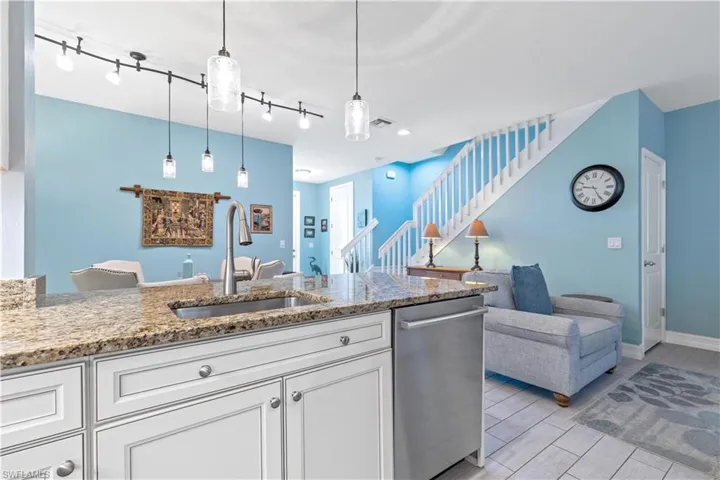 Kitchen with sink, hanging light fixtures, stainless steel dishwasher, light stone counters, and white cabinetry