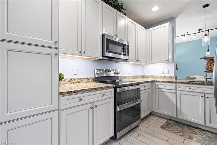 Kitchen featuring light stone countertops, rail lighting, stainless steel appliances, white cabinetry, and hanging light fixtures