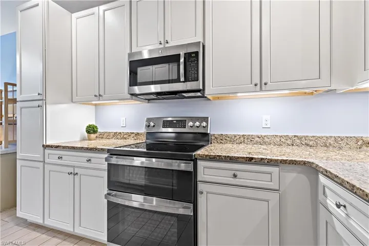 Kitchen with stainless steel appliances, white cabinetry, and light stone counters