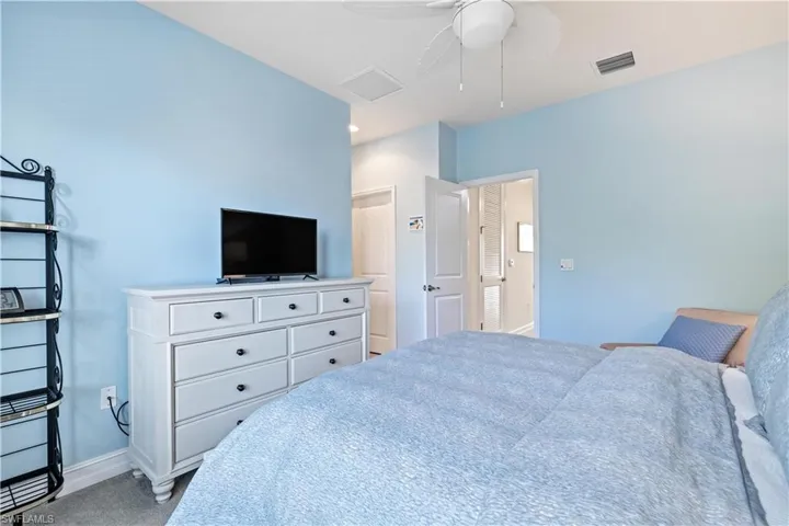 Corner view of primary bedroom eaturing ceiling fan and light carpet