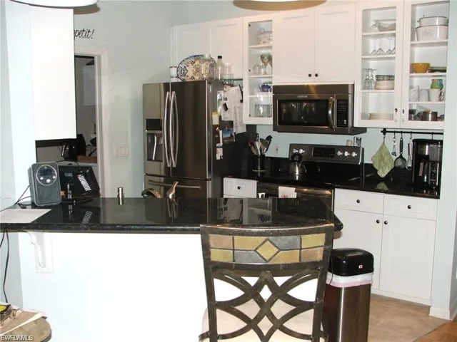 Kitchen with a kitchen breakfast bar, a peninsula, dark stone countertops, stainless steel appliances, and white cabinets