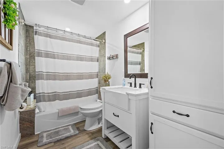 White shaker vanity with farmhouse sink, dark bronze fixtures, wood-finish flooring, built-in storage cabinetry, and subway tile shower surround