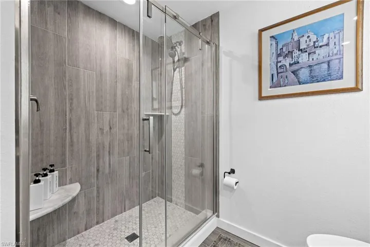 Glass-enclosed shower with a wood-look tiled wall and a hexagonal tile floor