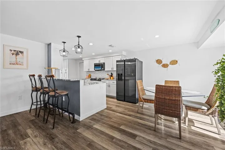 Open-concept kitchen featuring wood-finish flooring, white cabinetry, integrated appliances, and a breakfast bar with pendant lighting