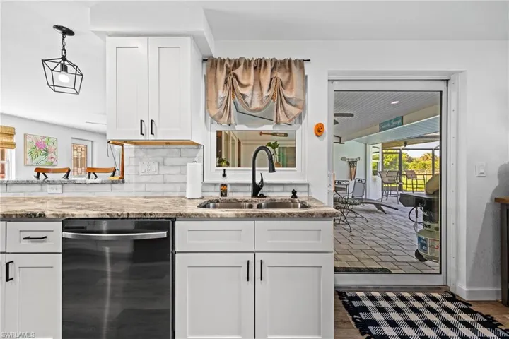 White shaker-style cabinetry with matte black hardware, stone-finish countertops, subway tile backsplash, and a built-in dishwasher