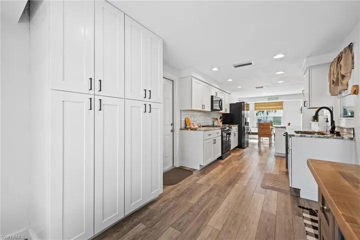 Crisp white cabinetry, wood-finish flooring, recessed lighting, and a white subway tile backsplash