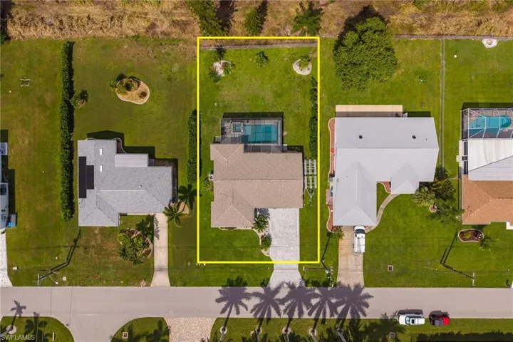 Aerial perspective showcasing a property with a swimming pool, paved driveway, and surrounding green lawn