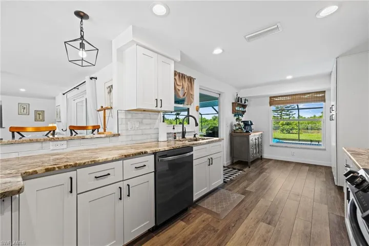 White cabinetry, wood-finish flooring, undermount sink with a matte black faucet, recessed lighting, and a window overlooking exterior landscaping