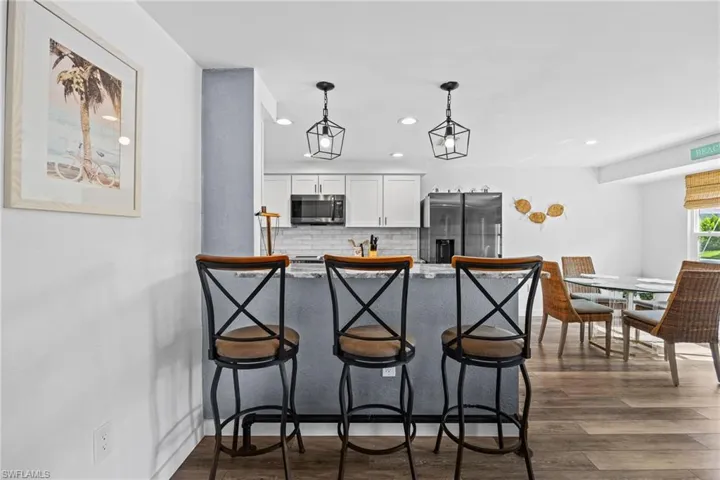Breakfast bar with pendant lighting, wood-finish flooring, white cabinetry, and stainless steel appliances