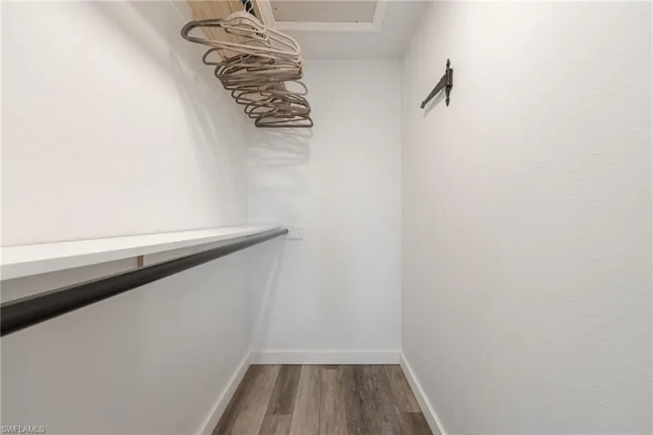Walk-in closet featuring a built-in shelf and hanging rod, complemented by wood-finish flooring