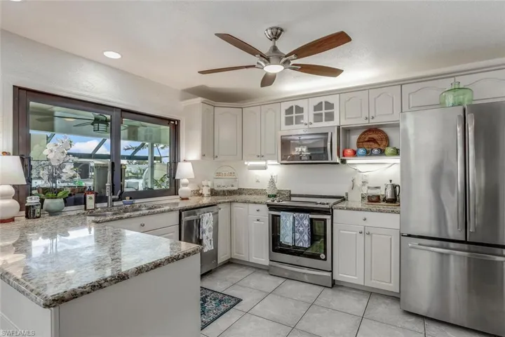 Kitchen with light stone countertops, sink, light tile patterned floors, white cabinets, and appliances with stainless steel finishes