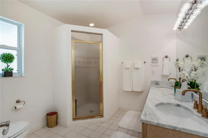 Bathroom featuring vanity, tile patterned floors, walk in shower, and vaulted ceiling