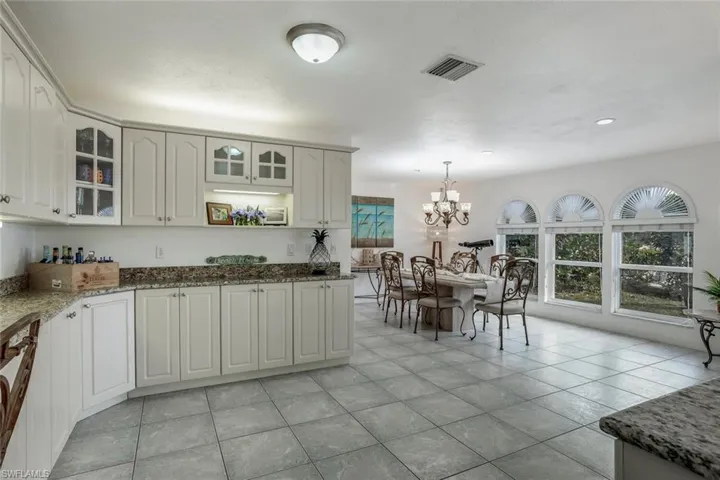 Kitchen with white cabinets, decorative light fixtures, light tile patterned flooring, and dark stone countertops