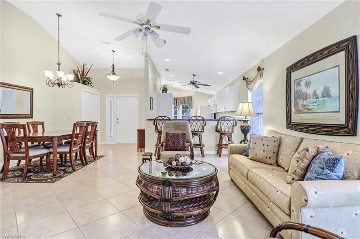 Living room featuring lofted ceiling, ceiling fan with notable chandelier, and light tile patterned floors