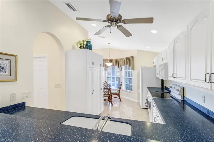 Kitchen featuring white appliances, sink, lofted ceiling, white cabinets, and light tile patterned floors