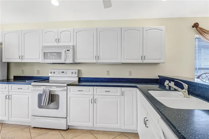 Kitchen with white appliances, light tile patterned floors, white cabinetry, and sink