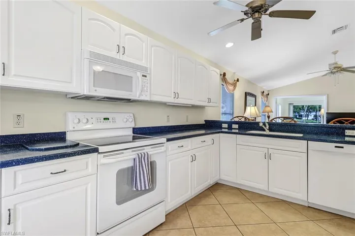 Kitchen featuring lofted ceiling, sink, light tile patterned floors, white cabinets, and white appliances