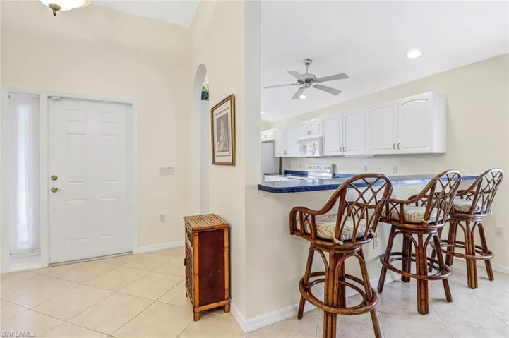 Kitchen with kitchen peninsula, white cabinets, ceiling fan, light tile patterned flooring, and white appliances