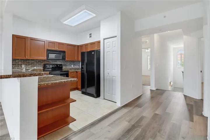 Kitchen featuring black appliances, tasteful backsplash, light wood-type flooring, dark stone countertops, and kitchen peninsula