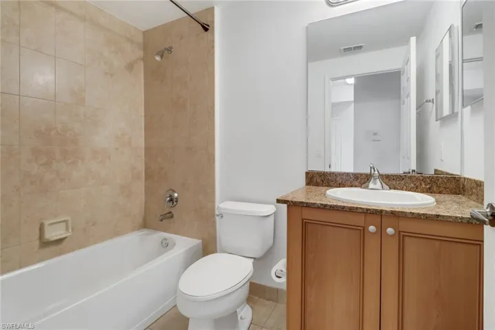 Full bathroom with toilet, tile patterned floors, tiled shower / bath combo, and vanity