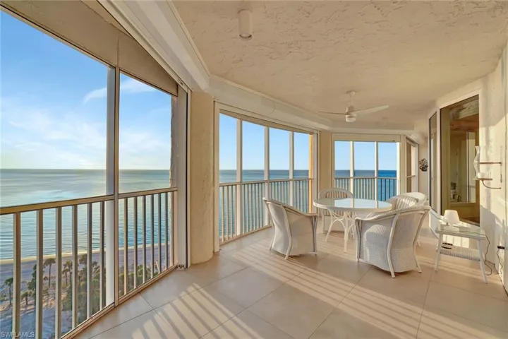 Sunroom with view of water and beach, tile patterned floors, and a textured ceiling