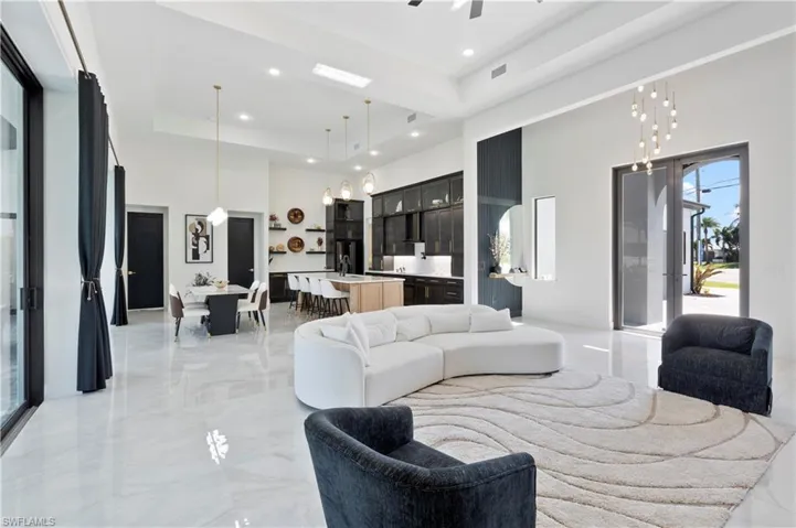 Living area with a raised ceiling, a towering ceiling, light marble finish flooring, recessed lighting, and a chandelier