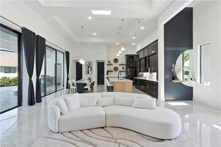 Living area with a high ceiling, a raised ceiling, light marble finish flooring, and recessed lighting