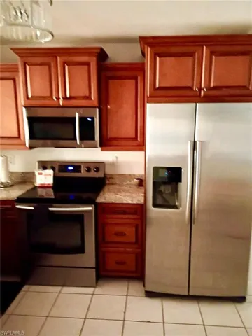Kitchen with stainless steel appliances, light tile patterned floors, and wood finish cabinetry