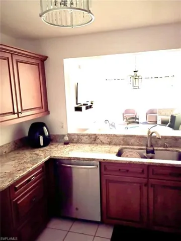 Kitchen featuring stainless steel dishwasher, light stone counters, light tile patterned floors, bold wood finish cabinetry, and suspended lighting