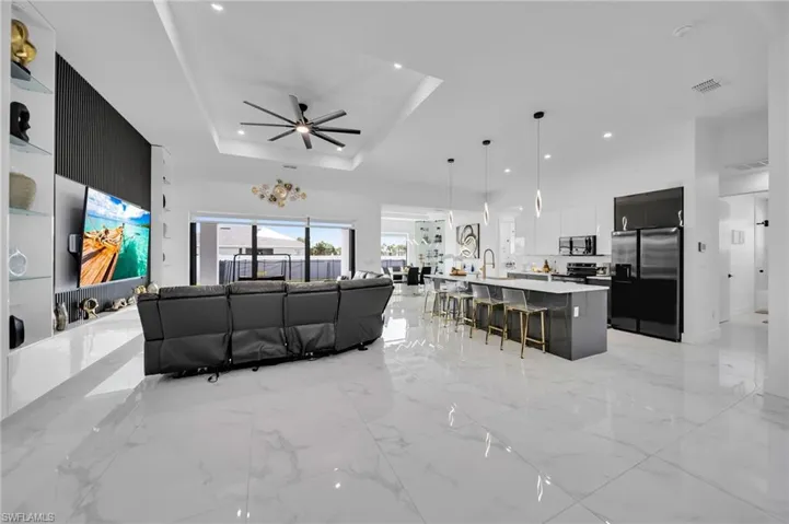 Living area featuring ceiling fan, recessed lighting, a tray ceiling, and light marble finish floors