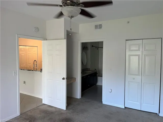 Unfurnished bedroom featuring a closet, sink, dark carpet, connected bathroom, and ceiling fan