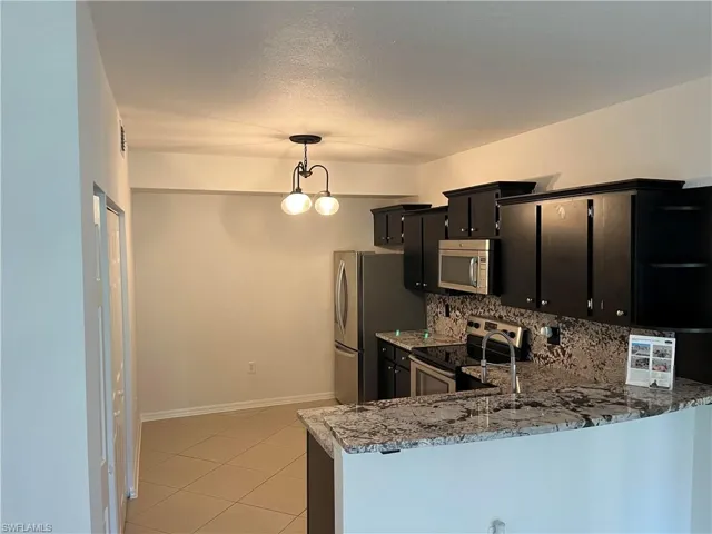 Kitchen with light tile patterned floors, kitchen peninsula, stainless steel appliances, decorative backsplash, and decorative light fixtures